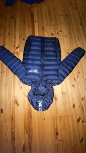 Marinblå Polo Club pufferjacka - Snygg marinblå pufferjacka från Polo Club med huva och logga på både bröstet och huvan. Jackan har dragkedja framtill, två sidofickor med dragkedja och quiltad design. Perfekt för kalla dagar och har en modern look som passar streetstyle.