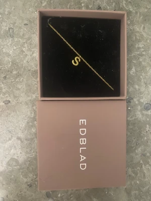 Guldigt halsband med S från Edblad - Snyggt och stilrent halsband från Edblad i guldton med ett hängsmycke i form av bokstaven S. Kedjan är tunn och elegant, perfekt för dig som vill ha något personligt och minimalistiskt. Kommer i original ask..