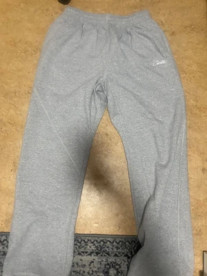 Grå mjukisbyxor från Corteiz XL - Säljer ett par grå mjukisbyxor från Corteiz i storlek XL. Byxorna har elastisk midja, fickor och vit broderad logga på framsidan. Materialet är mjukt och skönt, perfekt för chill dagar. Snyggt streetwear-plagg med enkel design och bekväm passform.