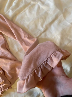 Rosa omlottopp med volanger från Gina Tricot - Supersöt ljusrosa omlottopp från Gina Tricot med långa ärmar och volangdetaljer längs halsringningen och ärmsluten. Toppen har snörning framtill. Pris kan diskuteras!!💕