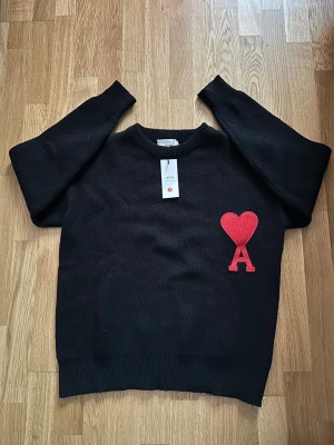 Svart stickad tröja från Ami S - Svart stickad tröja från Ami Alexandre Mattiussi i storlek S. Tröjan har ett rött broderat hjärta med bokstaven A på bröstet, rund hals och långa ärmar. Perfekt för dig som gillar stilrena detaljer och vill ha något som sticker ut. Pris går att diskutera dessutom om du vill ha mer bilder.
