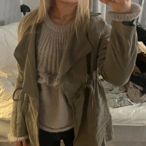 Olivgrön trenchcoat med snörning - Säljer en olivgrön trenchcoat med snygg snörning i midjan och breda slag. Jackan har lång ärm och en loose passform som ger en chill vibe. Perfekt för dig som gillar lager på lager och vill ha en stilren look. Materialet känns mjukt och har en matt finish.