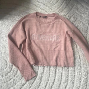 Rosa stickad tröja, Gymshark - Säljer en ljusrosa  stickad tröja från Gymshark med breda ribbade muddar och logga framtill. Tröjan har lång ärm och en relaxed fit som passar perfekt till träning eller chill. Storlek M