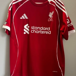 Liverpool röd matchtröja Adidas S - Liverpool FCs officiella matchtröja från Adidas i rött med vita detaljer och tryck. Kortärmad med Premier League-märke på ärmen, Aeroready-material för bra ventilation. Nummer 9 och namnet ISAK på ryggen. Snygga vita ränder på axlarna och klubbmärke på bröstet. Kan fixa fler bilder om man vill ha Helt oanvänd 