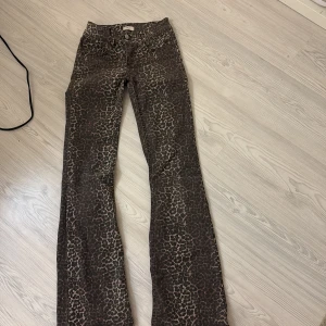Leopardmönstrade bootcut jeans Nelly - Snygga bootcut jeans från Nelly i leopardmönster. Byxorna är lågmidjade och har klassisk femficksdesign med dragkedja och dubbla knappar. Färgen är brun med svarta och beige detaljer. Perfekta för dig som vill sticka ut med en cool look.