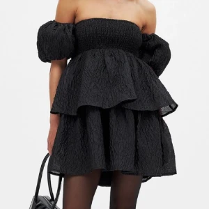 Na-KD klänning - Supersnygg svart kortklänning med puffärmar och stor rosett i ryggen. Klänningen har en offshoulder-design och är tillverkad i ett krinklat syntetmaterial som ger cool struktur. Volangdetaljer och omlottkänsla baktill gör den extra unik. Perfekt för dig som vill sticka ut.