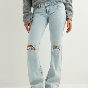 Ljusblå bootcut jeans från Nelly - Säljer mina Nelly jeans med hål, säljer eftersom att de är för långa och sitter lite löst på mig, skriv för egna bilder är säker på att de inte finns några defekter men kan vara lite slitna där nere då de är för långa. Kan också byta mot xs🩷