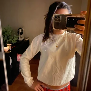 Vit sweatshirt med pärlor från H&M - Vit långärmad sweatshirt från H&M med pärldetaljer på axlarna. Tröjan har en klassisk rund halsringning och är gjord i mjukt material som känns skönt mot huden. Perfekt för dig som gillar en enkel men ändå lite extra look.