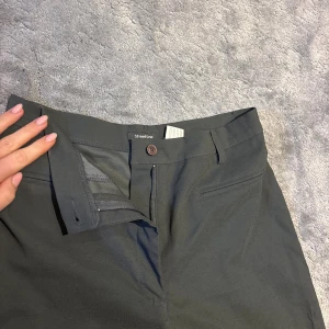 Mörkgrå/mötkgröna kostymbyxor från Street One - Snygga mörkgrå/mörkgröna kostymbyxor från Street One med främst raka men lite utsvängda ben och klassisk passform. Byxorna har hällor för bälte, diskreta fickor fram och stängs med knapp och dragkedja. 