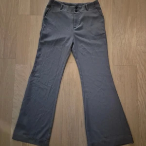 Grå bootcut byxor med knappar - Snygga grå bootcut byxor med två knappar framtill och fickor på sidorna. Byxorna har en klassisk passform med utsvängda ben