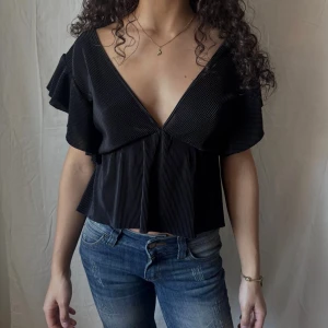 Svart v-ringad blus med volangärm  - Svart v-ringad blus med volangärmar, även v-ringad i ryggen. Funkar både till fest och till vardags.
