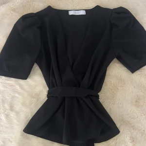 Svart omlottopp från Sisters Point - Svart omlottopp från Sisters Point med puffiga korta ärmar och band som man kan knyta i ryggen. 💞