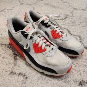 Nike Air Max 90 Gore-Tex sneakers - Nike Air Max 90 sneakers med Gore-Tex, i vitt, svart och rött. Klassisk siluett med synlig Air Max-dämpning, mesh och skinnpaneler samt röda detaljer på häl och snörning. Perfekta för dig som vill ha en ikonisk och vattentålig sneaker.