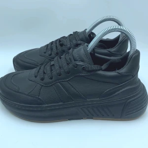 Svarta sneakers från Bottega Veneta - Chunky svarta sneakers från Bottega Veneta i skinn med bred platt sula och snörning. Snygga detaljer med logotyp på både plös och snören. Sulan är svart med kontrasterande bruna partier undertill. 