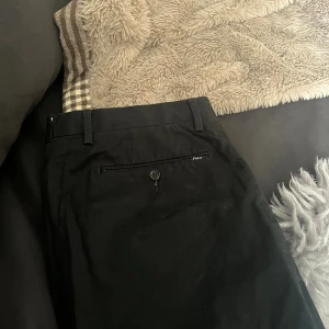 Polo Ralph Lauren, chinos, strl31/34 - Svarta chinos från Polo Ralph Lauren i stretchigt bomullsmaterial. Slim fit-modell med knapp och dragkedja fram samt bakficka med knapp. Klassisk och stilren design. De är luddiga men i övrigt är färgen bibehållen och tagits hand om väl.