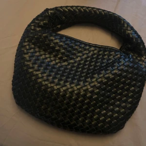 Svart flätad axelväska från NA-KD - Snygg svart axelväska från NA-KD med rundad form och flätad design. Ny och oanvänd 