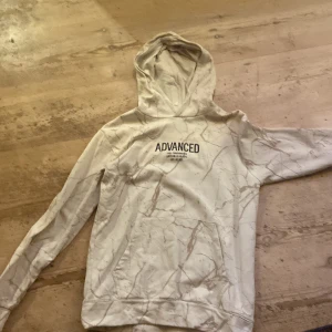 Vit hoodie med marmormönster Advanced - Säljer en vit hoodie från Ecode med marmormönster och trycket 'ADVANCED' på bröstet. Tröjan har huva, lång ärm och en stor magficka framtill. Perfekt för dig som gillar streetwear och snygga detaljer.