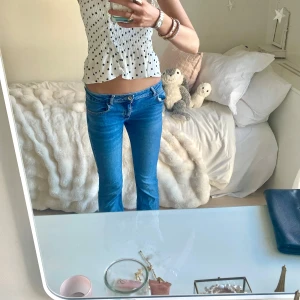Blå lågmidjade bootcut jeans - Säljer ett par blå jeans med låg/medel midja och bootcut-ben. Jeansen har klassisk femficksdesign och är tillverkade i ett stretchigt denimtyg som sitter snyggt på kroppen. Perfekta för dig som gillar en avslappnad men ändå trendig look. Långa i längden.