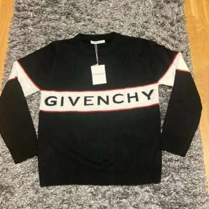 Svart stickad tröja från Givenchy  - Svart stickad tröja från Givenchy med vit panel och röd kant över bröstet där loggan är invävd. Långärmad modell med ribbade muddar och klassisk rund hals. Perfekt för dig som vill ha en stilren och lyxig look med tydlig logga.