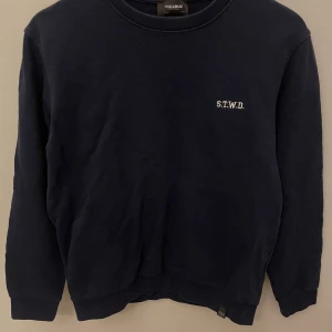 Mörkblå sweatshirt från Pull&Bear - Mörkblå sweatshirt från Pull&Bear med broderad vit text 'S.T.W.D.' på bröstet. Klassisk rund halsringning och långa ärmar. Perfekt basic-tröja med relaxed vibe, tillverkad i mjuk bomull för skön komfort.