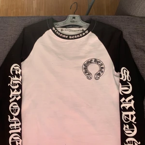 Chrome Hearts svartvit långärmad tröja - Säljer en svartvit långärmad tröja från Chrome Hearts med stora tryck på ärmarna och ryggen. Tröjan har kontrastfärgade svarta ärmar, vit kropp och coola logotyper både fram och bak. Tillverkad i 100% bomull och har en klassisk crewneck.