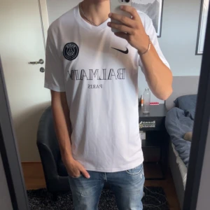 PSG x Balmain Kit - Snygg vit PSG x Balmain fotbollströja från Nike. Tröjan har korta ärmar och är tillverkad i Dri-FIT-material för optimal komfort. Den har PSG-loggan och Balmain Paris-tryck på framsidan. Perfekt för fotbollsfans som vill ha stil på planen. Nyskick!