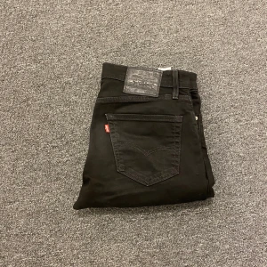Svarta Levi's 511 jeans slim fit - Svarta Levi's 511 jeans med slim passform och klassisk femficksdesign. Jeansen har en svart läderpatch med logga bak och den ikoniska röda Levi's-taggen på bakfickan. Materialet är mjukt jeans och midjan är normal. Perfekt för dig som gillar stilrena och enkla svarta jeans.