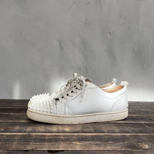 Vita Christian Louboutin sneakers - Unika vita sneakers från Christian Louboutin med nitar och den klassisk röd sulan. Skorna är inte i perfekt skick men fortfarande riktig cleana. Skorna har en fläck med förg som lossnat men som jag har målat över med vit skofärg bild finns i dm. Passar med vad som helst. Skriv om ni har frågor eller om ni vill ha fler bilder! 👌