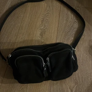 Svart axelväska från Gina Tricot - Svart axelväska med flera fack och silvriga dragkedjor från Gina Tricot. Väskan har en justerbar axelrem och en extra rem med nitar för att byta stil. Perfekt storlek för mobilen, plånboken och smågrejer. Snygg och praktisk för dig som gillar att ha koll på dina saker.