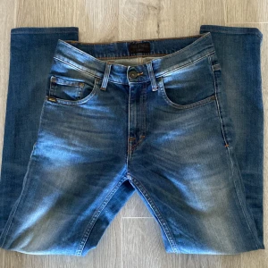 Blå jeans från Tiger of Sweden - Snygga blå jeans från Tiger of Sweden med klassisk femficksdesign och orangea kontrastsömmar. Jeansen är slim fit passform och är tillverkade i slitstarkt denimtyg. Perfekta för dig som gillar stilrena och tidlösa jeans.