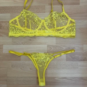 Nya. Gul broderad spets bralette - Superfin gul bralette i transparent mesh med broderade blommor och tunna axelband. Spetsdetaljer längs kanterna och justerbara band för perfekt passform. Matchande stringtrosa med samma broderade blommönster ingår. Förminskad som L