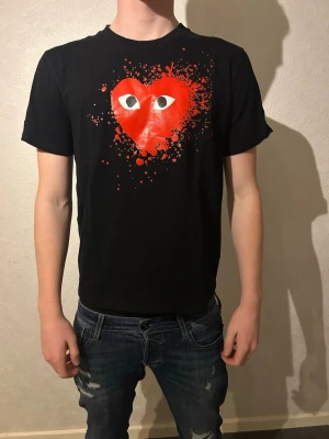 Svart Comme des Garçons Play t-shirt - Svart t-shirt från Comme des Garçons Play med ikoniskt rött hjärta med ögon och coolt splattertryck på bröstet. Klassisk passform och rund hals. Har kvar lappen.