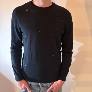 Mörkblå tröja från Massimo Dutti - Snygg mörkblå tröja från Massimo Dutti i extrafin bomull. Tröjan har diskreta små broderade detaljer i blått och vitt samt rund halsringning och långa ärmar. Perfekt för dig som gillar stilrena plagg.