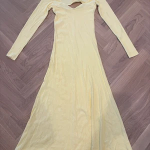 Ljusgul långklänning från Vero Moda - Supersnygg ljusgul långklänning från Vero Moda med ribbad struktur och lång ärm. Klänningen har en cool v-ringad detalj med cut-out vid halsen som ger en trendig touch. Materialet är mjukt och stretchigt, perfekt för dig som gillar bekväma och stilrena plagg.