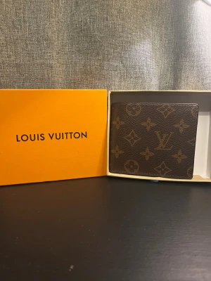 Brun monogram plånbok - Säljer en klassisk brun plånbok med ikoniskt monogrammönster. Plånboken är i skinn och har flera kortfack, fönster för ID och plats för sedlar. Kommer i original orange box. Perfekt accessoar för dig som gillar lyxig och tidlös stil.