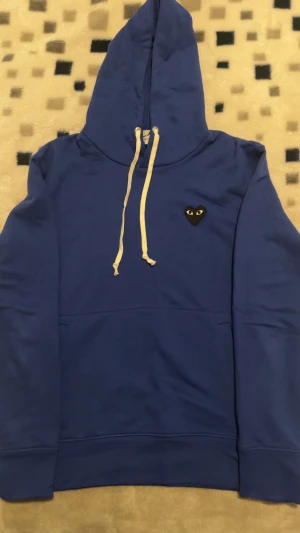 Comme des Garçons Hoodie  - Snygg blå hoodie från Comme des Garçons med det klassiska hjärt-loggan på bröstet. Mjukt material, vita dragsnören och perfekt passform. I mycket fint skick och knappt använd. Passar både herr och dam!