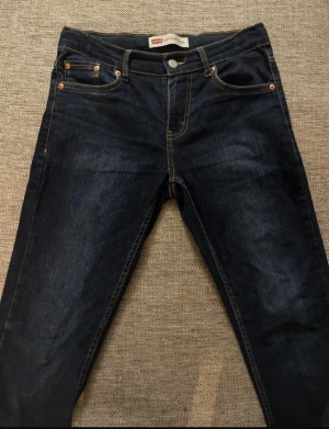 Levi's 512 Slim Taper jeans mörkblå - Mörkblå Levi's 512 Slim Taper jeans med klassiska fem fickor, gul kontrastsöm och snyggt taperat ben. Jeansen har en slim passform och är tillverkade i robust denim med detaljer i kopparfärg. Går även att sjustera storleken i midjan.