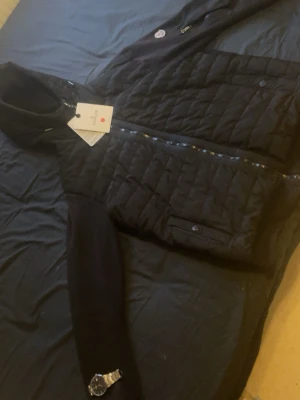 Moncler Cardigan (Svart) - Svart dunväst från Moncler med quiltad framsida och snygga detaljer. Västen har dragkedja och praktiska fickor med knappstängning. Perfekt för lager-på-lager och har en stilren look som funkar till många outfits.