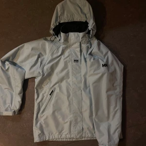 Ljusgrå vindjacka Helly Hansen XL - Snygg ljusblå skaljacka från Helly Hansen i storlek XL men passar mer som en L. Perfekt för blåsiga dagar och har nyligen tvättat och impregnerat den så borde funka bra i regnet eller i skidbacken. Kom me bud om du vill