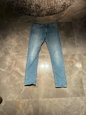 Levi's 511 ljusblå skinny jeans - Säljer ett par Levi's 511 jeans i ljusblå tvätt med klassisk femficksdesign och brunt läderpatch bak. Jeansen har smal passform och raka ben, tillverkade i mjukt jeanstyg med stretch för extra komfort. Perfekt för dig som gillar en clean och modern look.