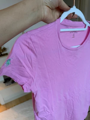 Rosa t-shirt från Ralph Lauren - Snygg rosa t-shirt från Ralph Lauren i mjuk bomull. Klassisk rund hals och korta ärmar med den ikoniska gröna Polo-loggan broderad på vänster ärm. Perfekt för dig som gillar stilrena och färgglada plagg.