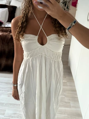 Vit långklänning med omlottband - Säljer en vit långklänning med omlottband över bröstet och snygg cutout-detalj framtill. Klänningen har en luftig passform och är ärmlös med smala axelband som korsas i halsen. Från hm sitter som en s 