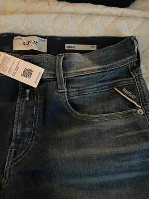 “Replay Anbass, helt nya med prislapp, aldrig använda. Nypris 1 699 kr!! - ( Längd 32 waist 29) Riktigt Snygga Replay Anbass slim fit jeans i en tvättad blå färg med klassiska fem fickor och läderpatch bak. Jeansen har en smal passform och subtila slitningar för en modern look. Perfekta för dig som gillar stilrena och bekväma jeans med cool attityd.