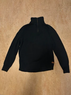 Svart stickad polotröja Peak Performance - Snygg svart stickad polotröja från Peak Performance med ribbad krage, muddar och nederkant. Tröjan har långärmad design och är perfekt för kyliga dagar. Klassisk och stilren look med diskret Peak Performance-märke vid nederkanten. Den är i nyskick men har ej prislapp eller orginialförpackning