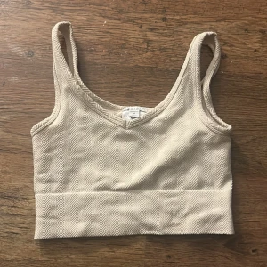 Beige linnetopp med fiskbensmönster - Säljer en beige linnetopp från Amisu med snyggt fiskbensmönster. Toppen är ärmlös och har breda axelband samt en croppad passform. Materialet är mjukt och känns lyxigt mot huden, perfekt för att lyfta din outfit med en cool detalj. Lite nopprig annars fick skick. Jätte skönt material