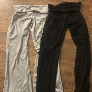 Svarta och gråa mjukisbyxor - Två par mjukisbyxor i svart och grått, med bred linning och raka ben. Perfekta för chill eller träning, tillverkade i mjukt syntetmaterial som känns skönt mot huden. Snygg enkel design utan synliga detaljer eller mönster. ”Yogapants” stl M men skulle snarare säga xs/S