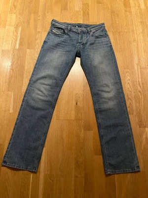 Blå raka jeans från Diesel - Snygga blå jeans från Diesel med klassisk femficksdesign och raka ben. Jeansen har en ljus tvätt och Diesel Industry-detalj på myntfickan. Tillverkade i bomull för en skön känsla och stilren look. De är sprillans nya utan prislapp. Modell: 1985 Larkee. Storlek: 33/34. Nypris: 1499.