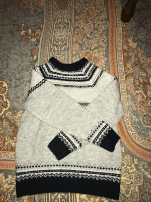 Grå stickad tröja från Esmara - Säljer en grå stickad tröja från Esmara med mörkblå och vita detaljer i ett snyggt mönster runt halsen, ärmsluten och nederkanten. Tröjan har långärmad passform och ribbade muddar. Perfekt för kalla dagar och riktigt mysig stil.