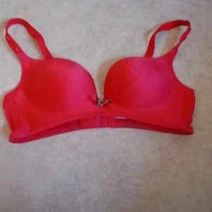 Röd BH  - Cool röd BH  med vadderade kupor och justerbara axelband. Toppen har flera hakknäppningar bak för perfekt passform och en liten metall-detalj framtill. Snygg och figurnära modell som ger en riktigt trendig look.