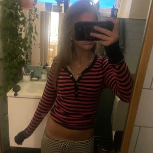 Randig långärmad tröja Gilly Hicks - Säljer en långärmad tröja från Gilly Hicks i svart och rosa med smala ränder. Tröjan har knappar vid halsen, svarta muddar och liten broderad GH-logga på bröstet. Modellen är figurnära och passar perfekt till jeans eller kjol. Storlek L men passar m och s